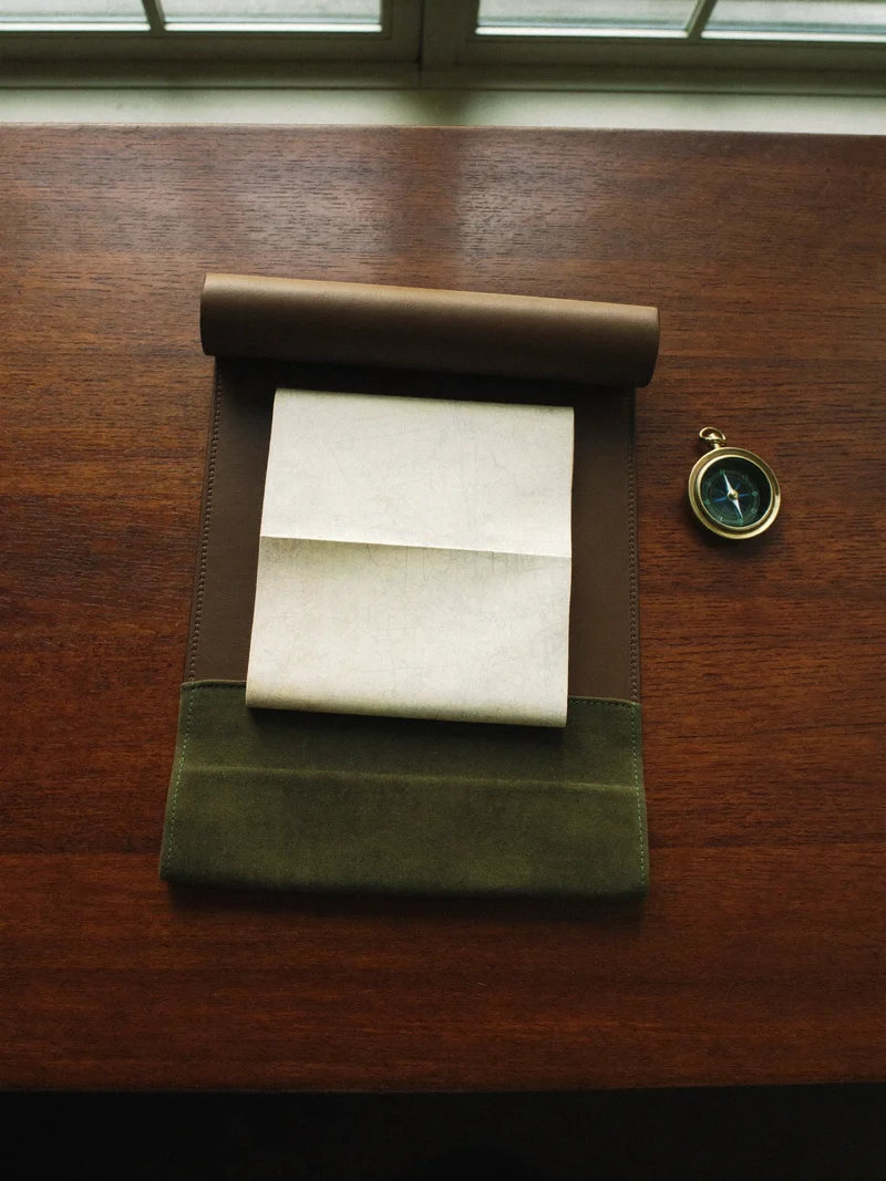 Aufgerolltes Etui aus Leder und Canvas mit Papierkarte und Messingkompass auf einem Holztisch