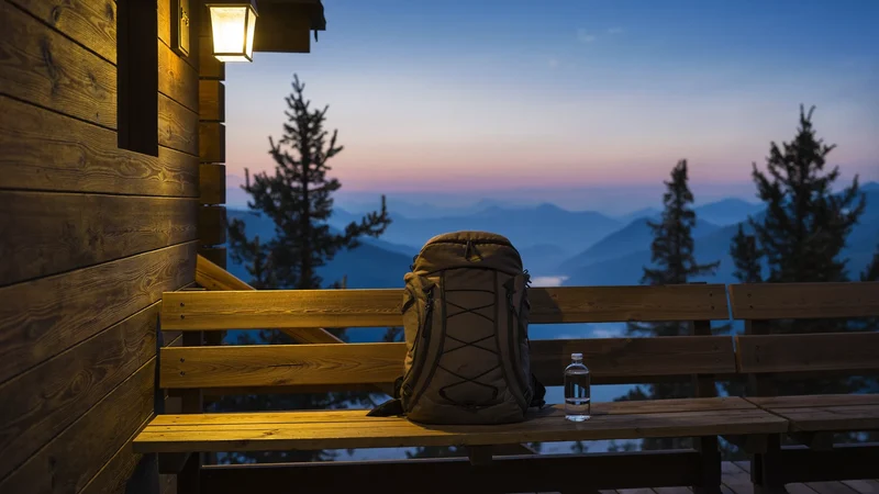Holzterrasse einer kleinen Berghütte in der Dämmerung mit Rucksack und Flasche